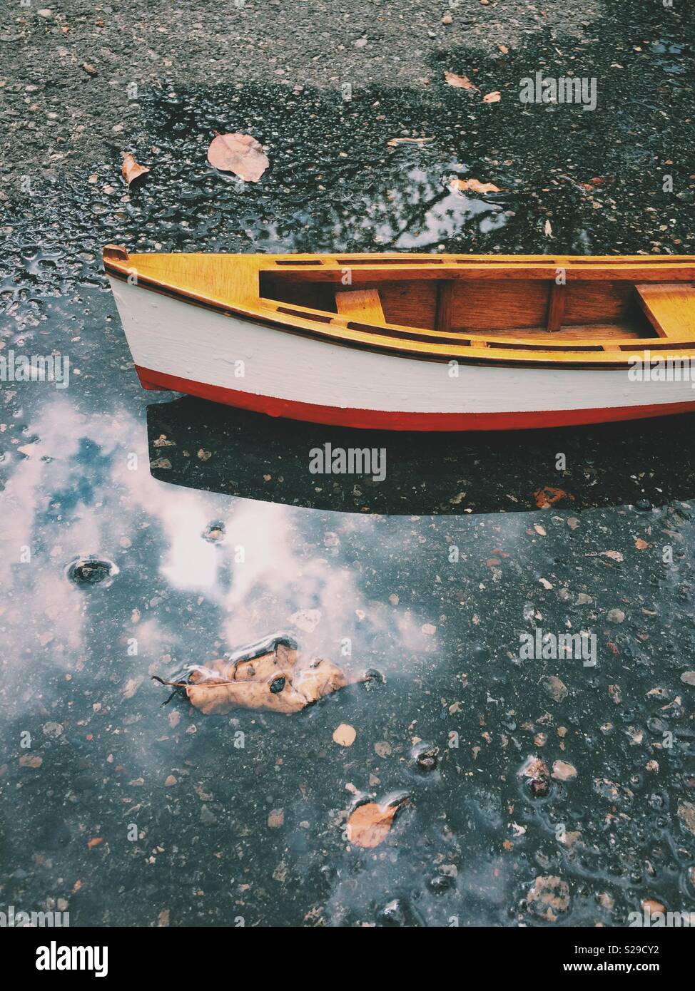 Wooden toy row boat floating in puddle with reflection. Stock Photo