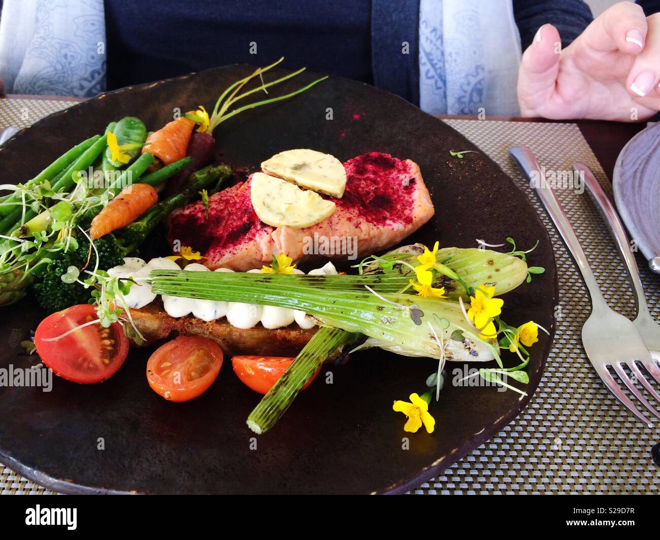 Grilled Salmon and colourful accompanied vegetables and edible flowers on black serving plate as main meal Stock Photo