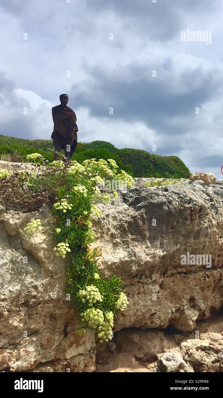 Blackman loocking to the menorca’s horizon, standing up a rocky point wearing a towell Stock Photo