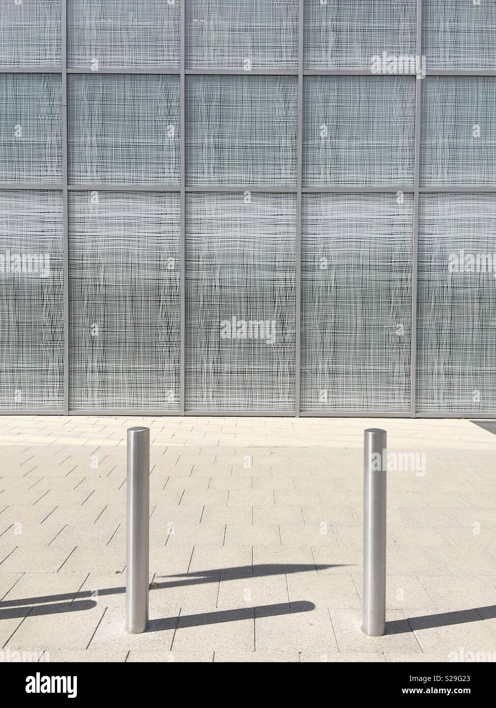 An urban environment with silver bollards protecting a path in front of a large retail store window with a minimalist feel - Smartphone Captured Stock Image