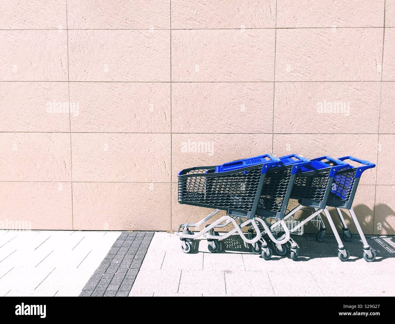 A line of shopping trolleys in front of a large wall outside a retail store in a minimalist environment - Smartphone Captured Stock Image