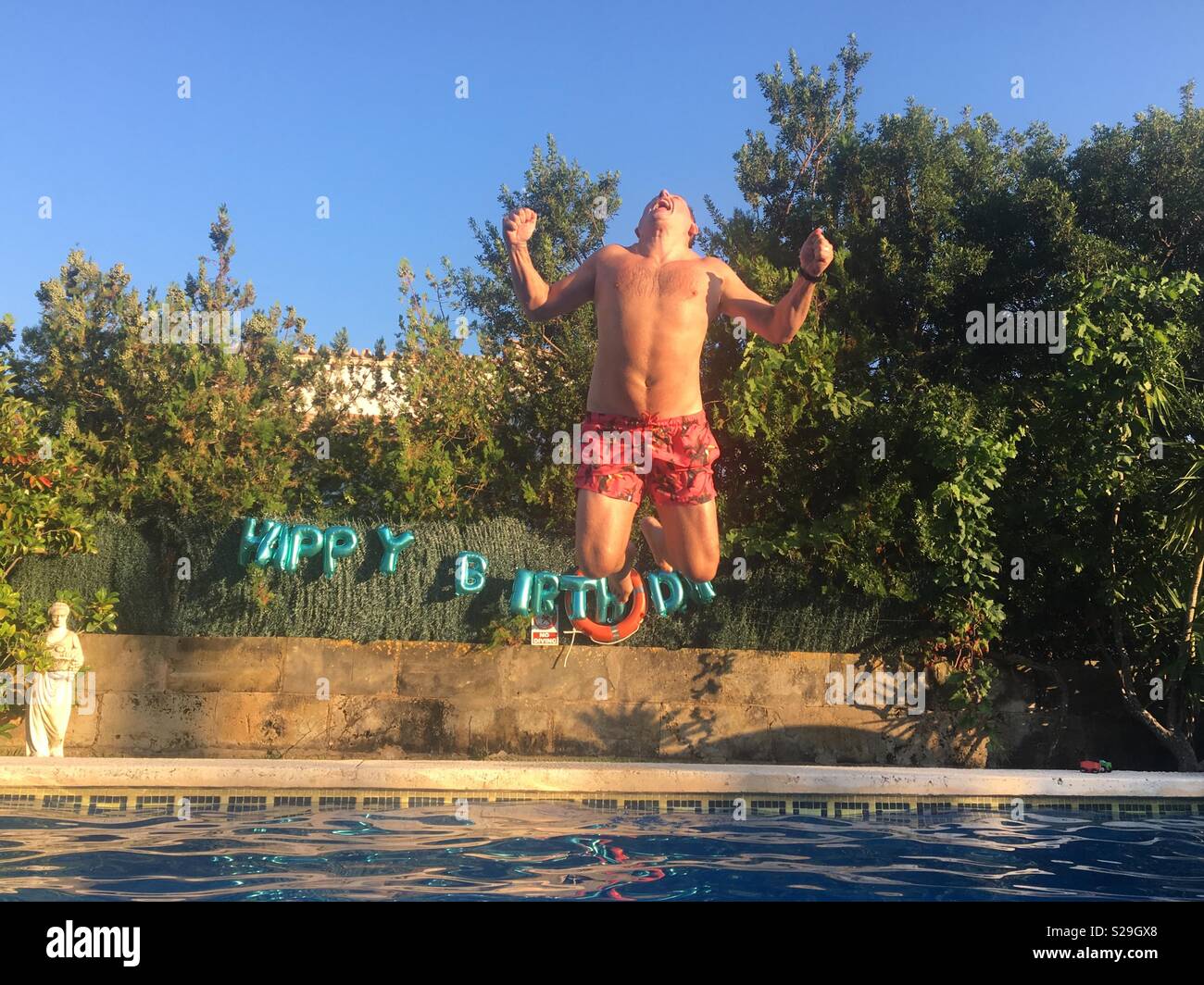 Man celebrating his birthday by jumping into a swimming pool Stock Photo