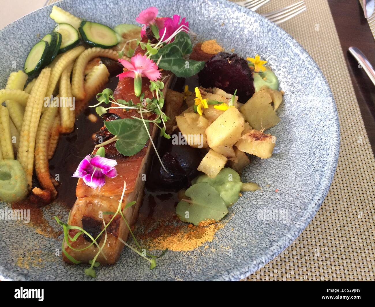 Pork belly grilled to perfection and served with an assortment of colorful vegetables and edible flowers at an upmarket restaurant at lunch Stock Photo