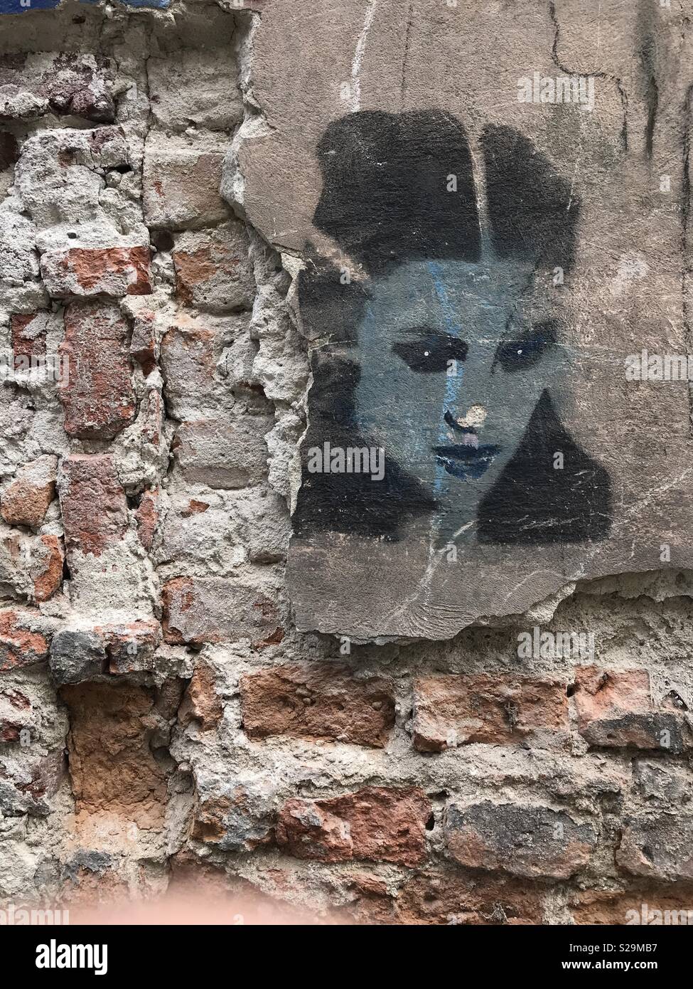 Black and white stencil art depicting the portrait of a young lady, on a crumbling brick wall with concrete render, located in the Polish city of Kraków. Stock Photo