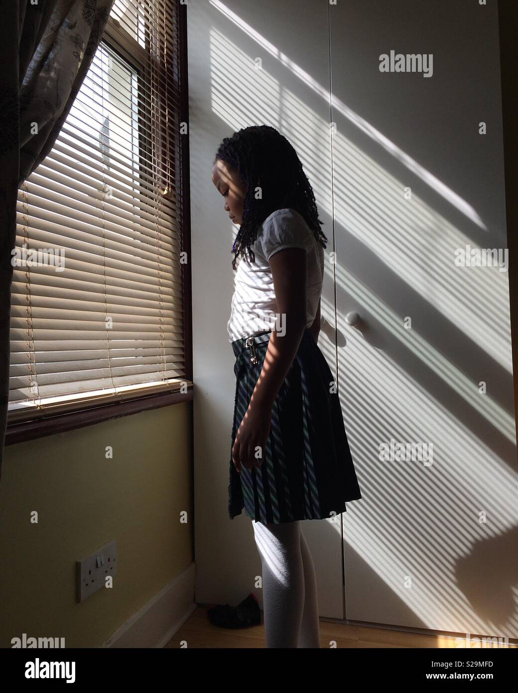 Girl in a kilt standing in the sun coming through a window Stock Photo