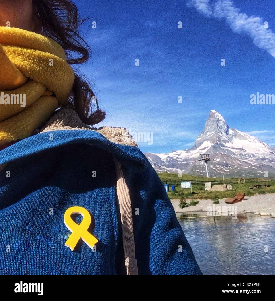 Catalan tourist with a yellow ribbon pinned in her blue jacked  in support of jailed pro-independence Catalan politicians . View of Matterhorn, Zermatt, Wallis or Valais, Switzerland Stock Photo