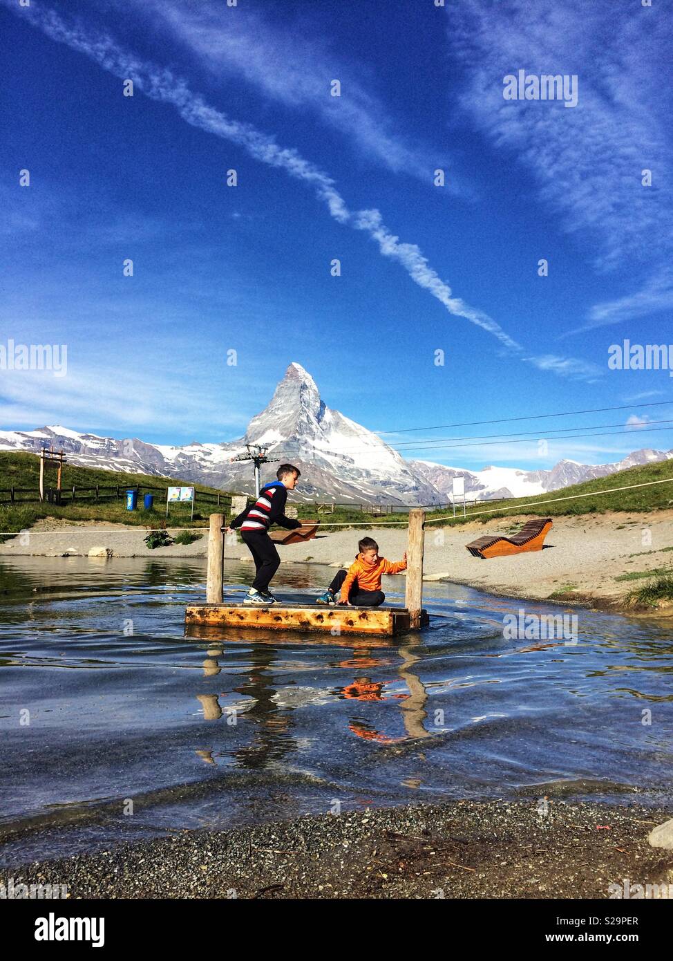 Two childs crossing Leisee lake, Sunegga, Rothorn Paradise: one of top five lakes destination around Natterhorn Peak in Zermatt, Switzerland, Europe - Smartphone Captured Stock Image