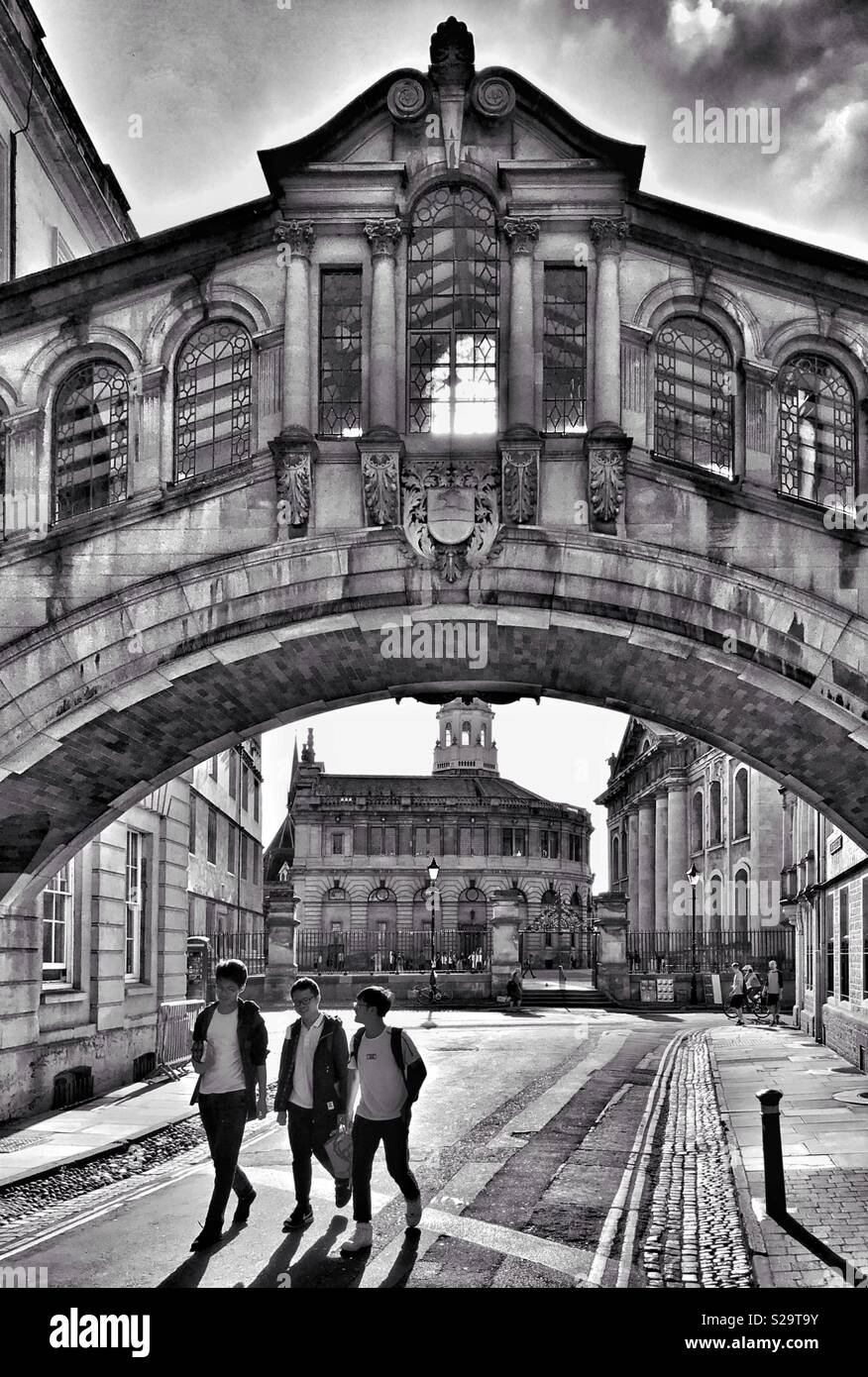 Three friends walk underneath the famous “Bridge Of Sighs” in Oxford, England. The famous Hertford Bridge landmark links the Old & New Quadrangles Of Hertford College. Photo Credit - © COLIN HOSKINS. - Smartphone Captured Stock Image