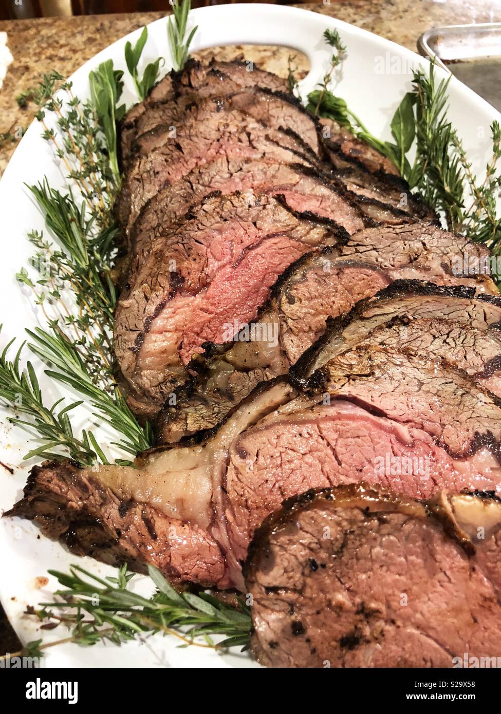 Beautiful slices of prime rib meat on a white platter garnished with rosemary. Stock Photo
