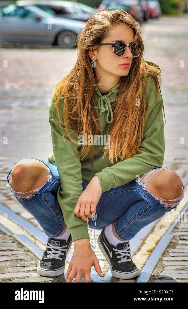 Teenage girl with ripped jeans and sunglasses squat down on tram track  Stock Photo - Alamy