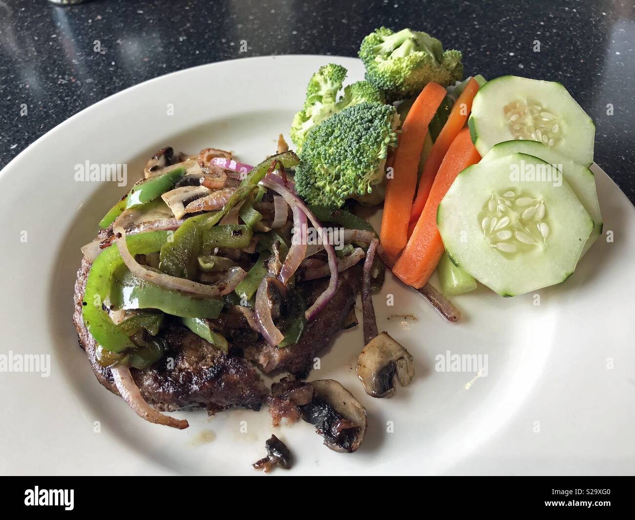 Low carb meal of hamburger topped with grilled onion, bell pepper and mushrooms with a side of raw broccoli, cucumbers, carrots and red bell peppers. Stock Photo