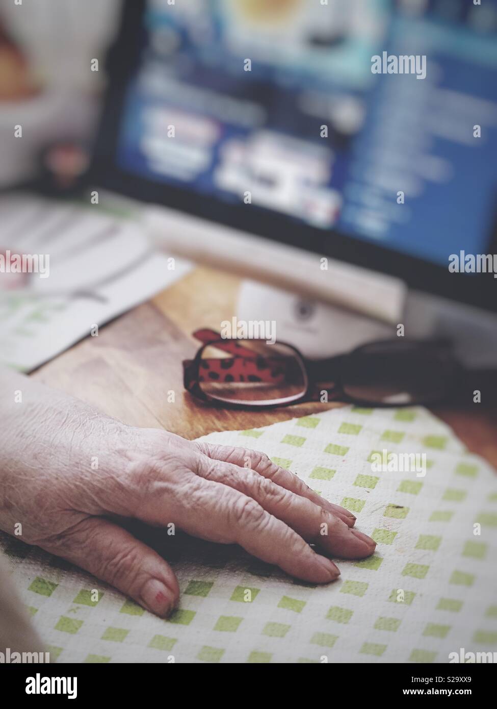 A senior woman wrinkled hand on a everyday table close to an ipad live streaming television - Smartphone Captured Stock Image