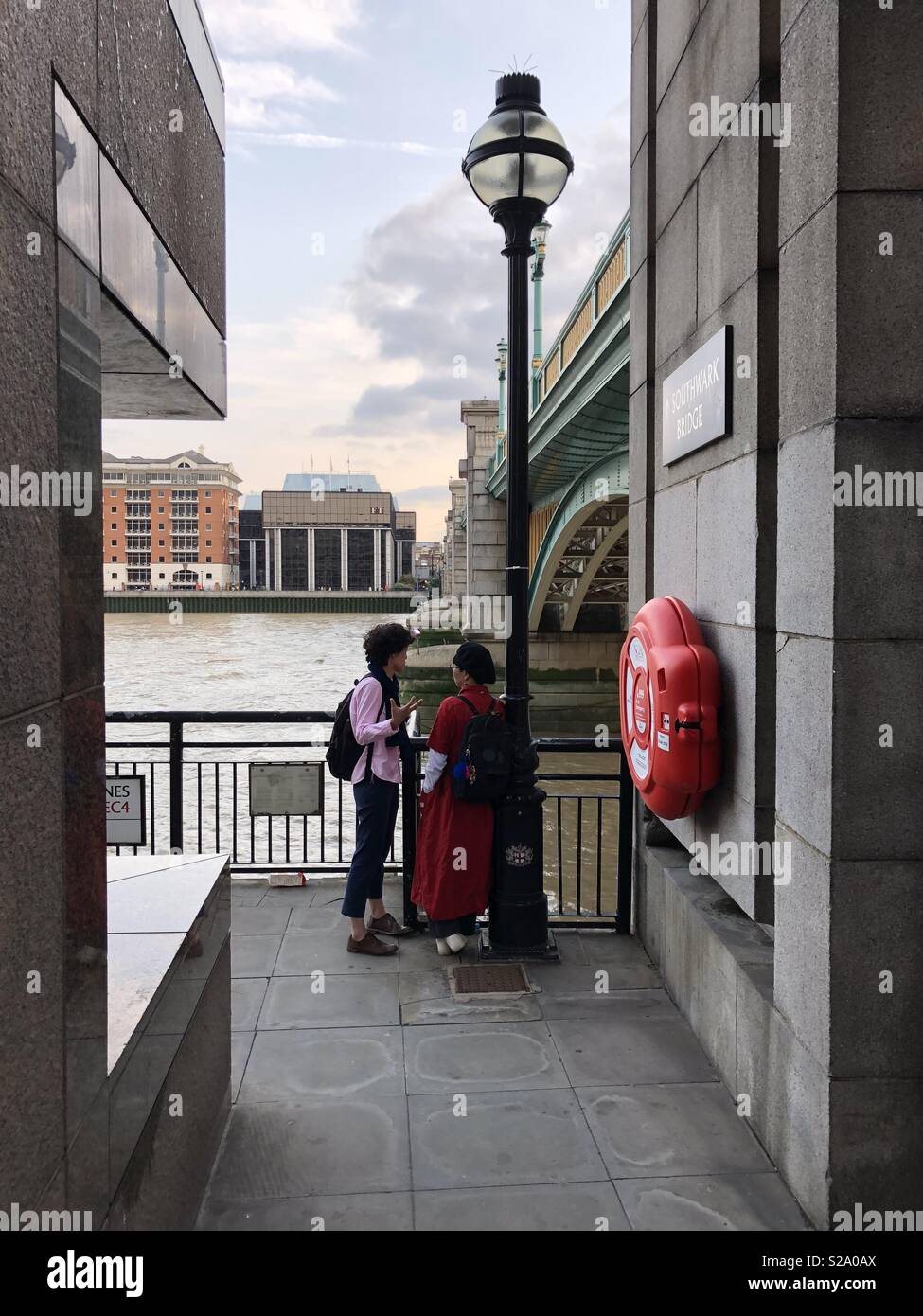 Two women in conversation by lamp post next to Southwark bridge London with river Thames in background Stock Photo
