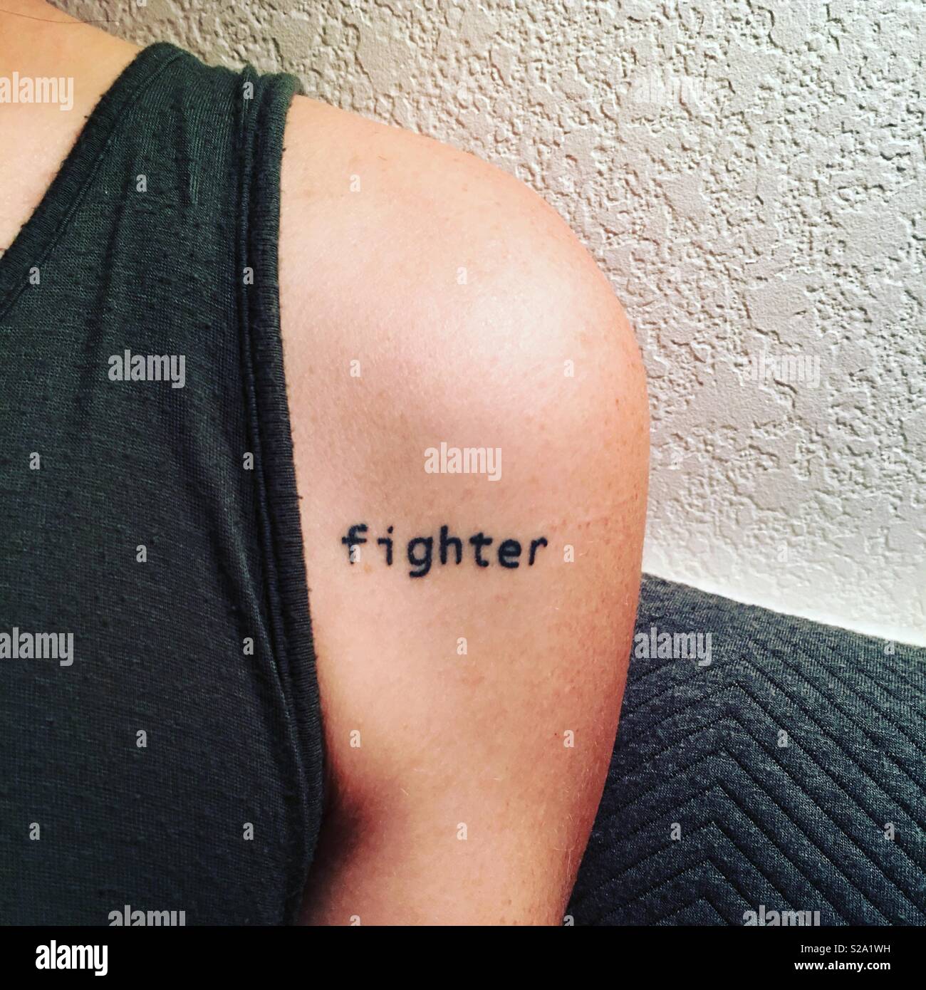 A woman’s shoulder with a tattoo that reads “fighter.” Stock Photo