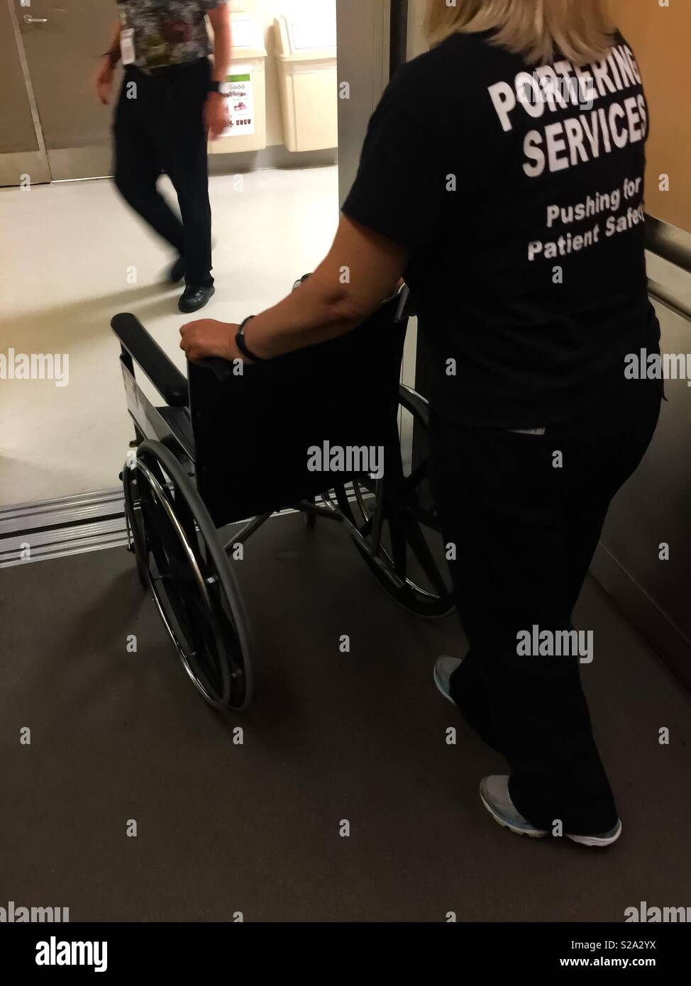 Portering. We push everyone around. A porter pushing a wheelchair out of an elevator at a medical facility, Ontario, Canada. Mobility assistance. - Smartphone Captured Stock Image