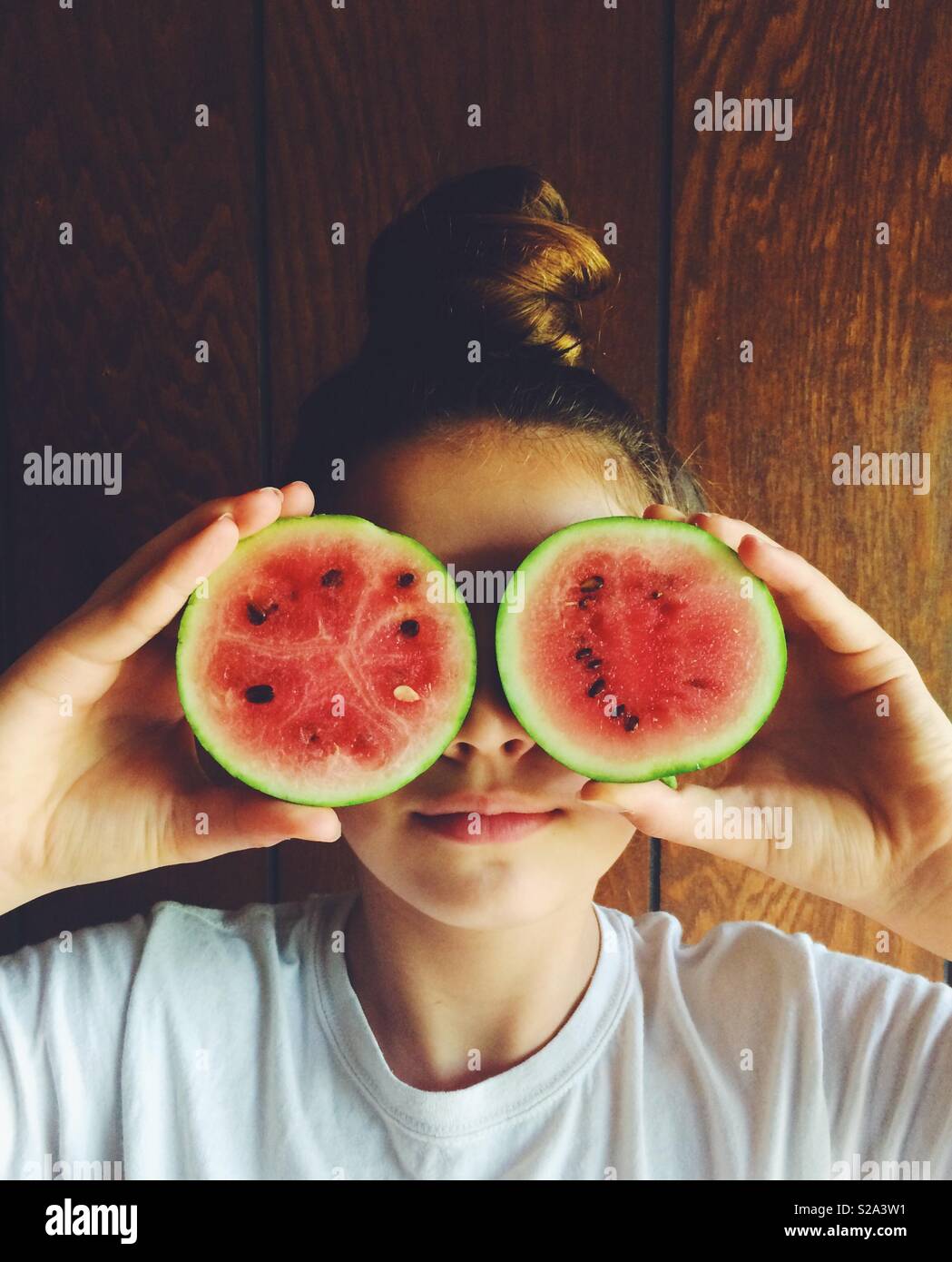 Smiling preteen brunette girl with two mini red watermelons in front of her eyes. Stock Photo