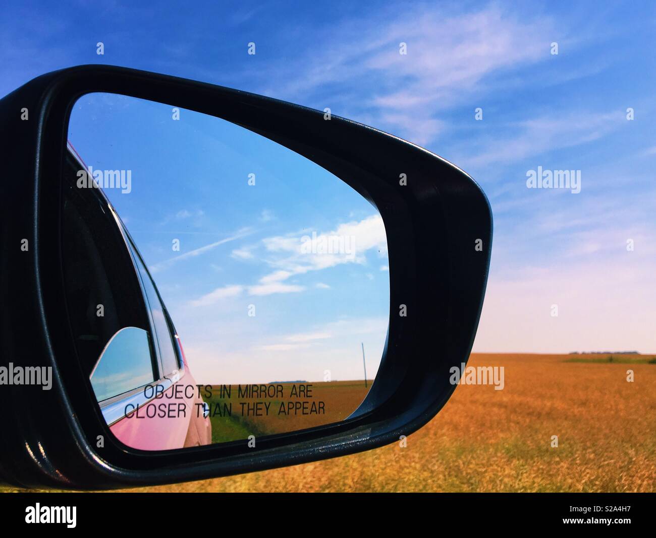 Review mirror of a car with the view of field and blue sky. Room for copy. Stock Photo