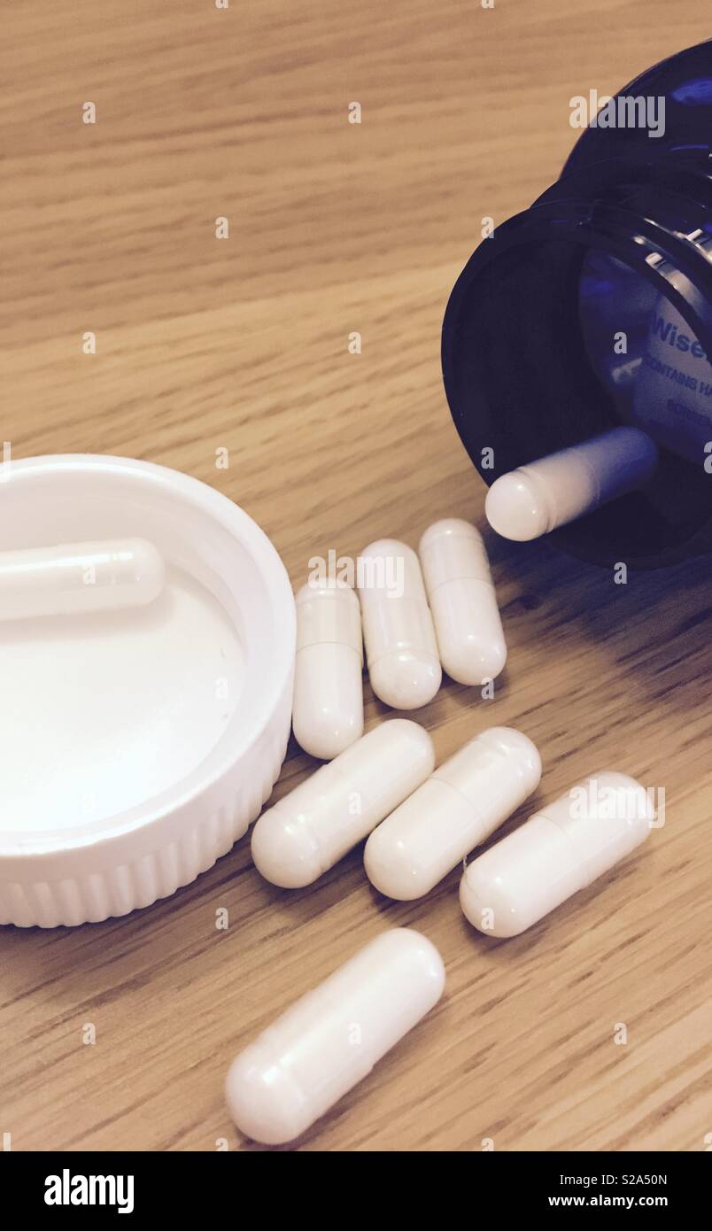 White medicine capsules falling out of a blue pill bottle on wooden table  Stock Photo - Alamy