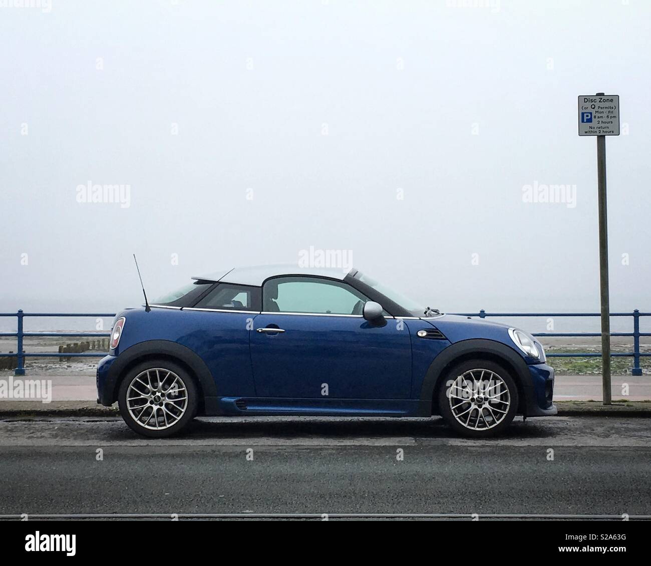 Blue and silver Mini against a misty gray background parked on Douglas promenade, Isle of Man. Stock Photo