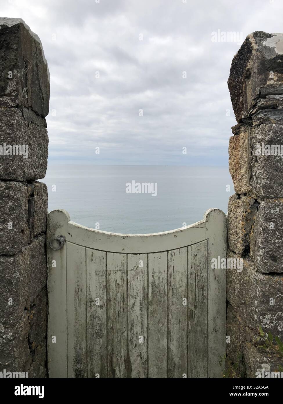 Gate in between stone wall overlooking the sea Stock Photo
