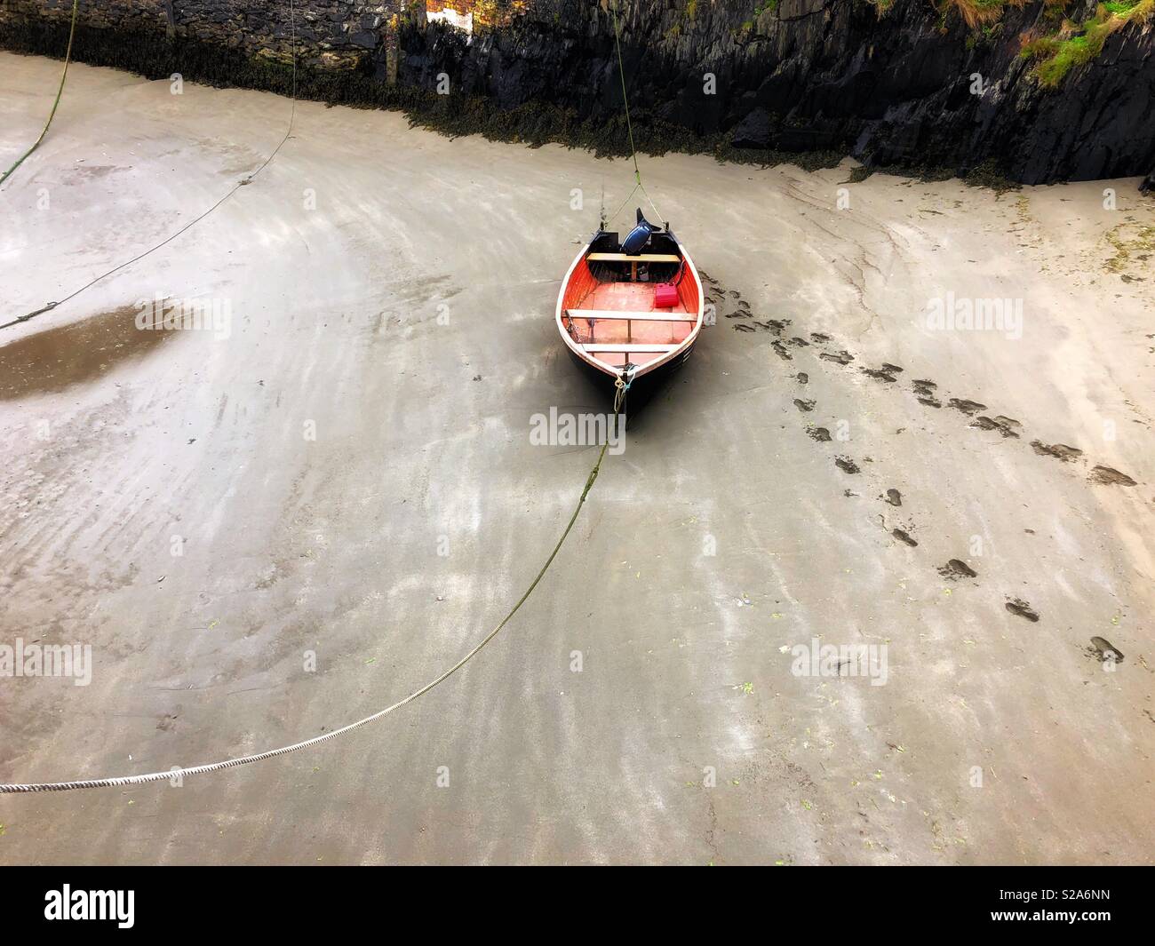 Lone rowing boat moored in Porthgain Harbour, Pembrokeshire, West Wales, with foot prints leading to and from the boat. - Smartphone Captured Stock Image