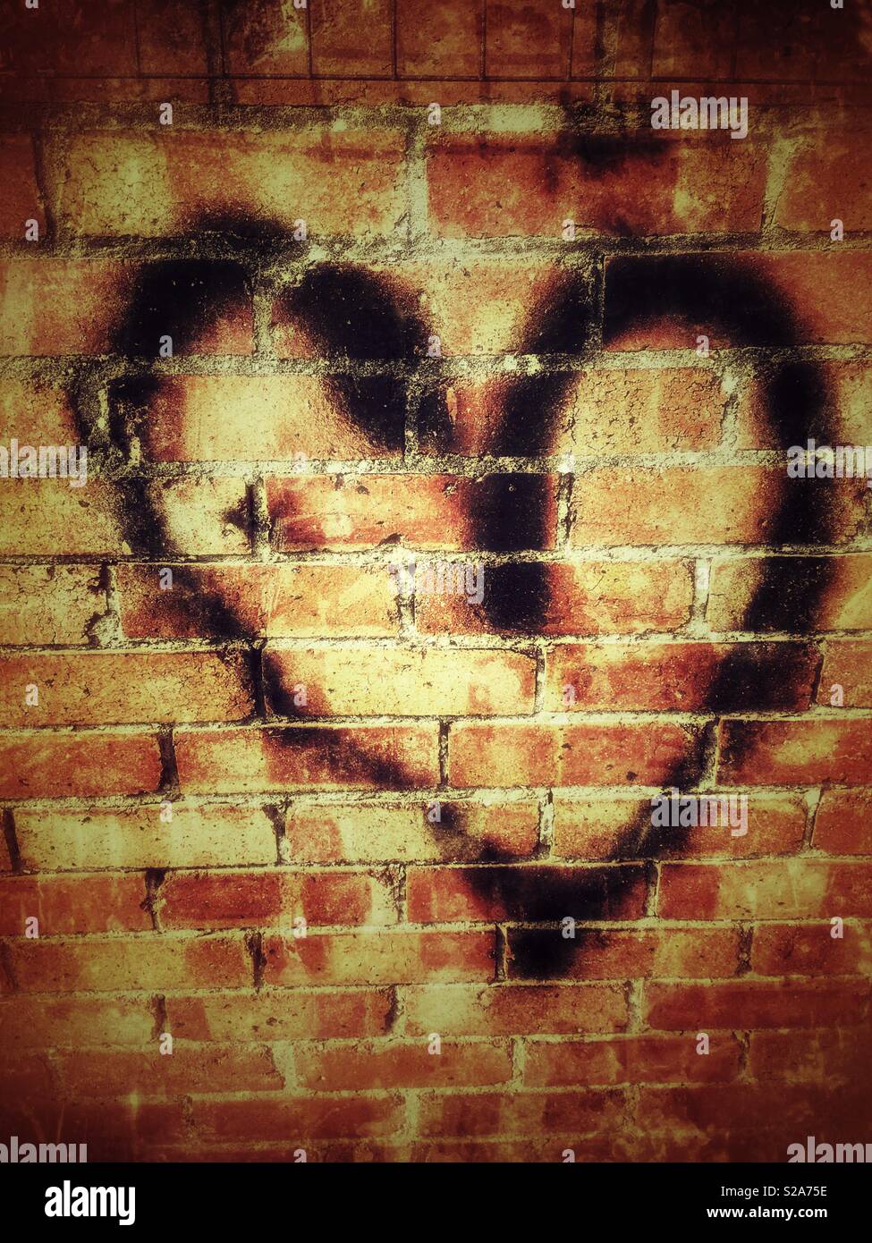 Black heart shape in paint sprayed on a red brick wall Stock Photo