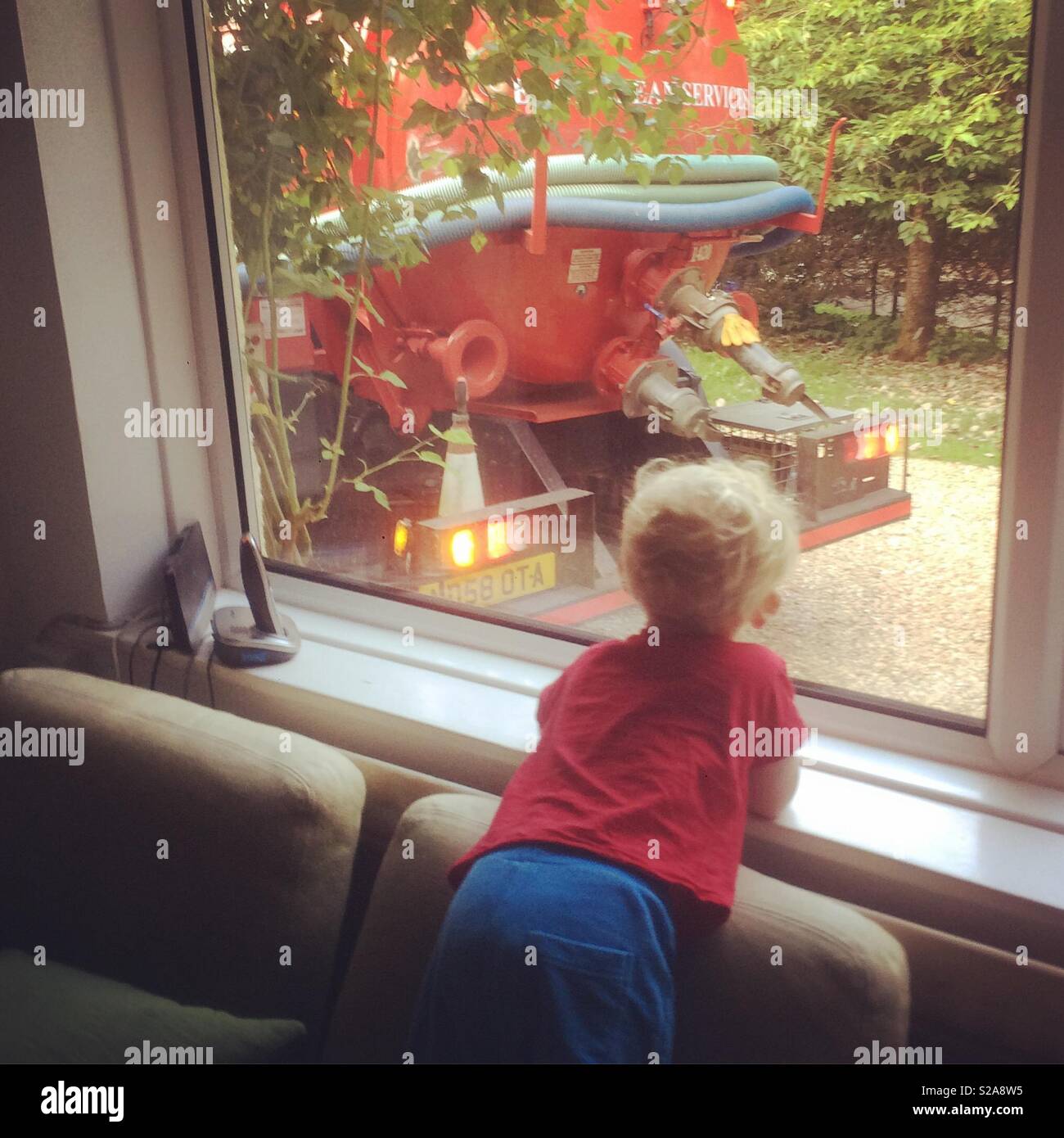 Two year old boy watching a sewage tanker truck through a window, Medstead, Hampshire, England. Stock Photo