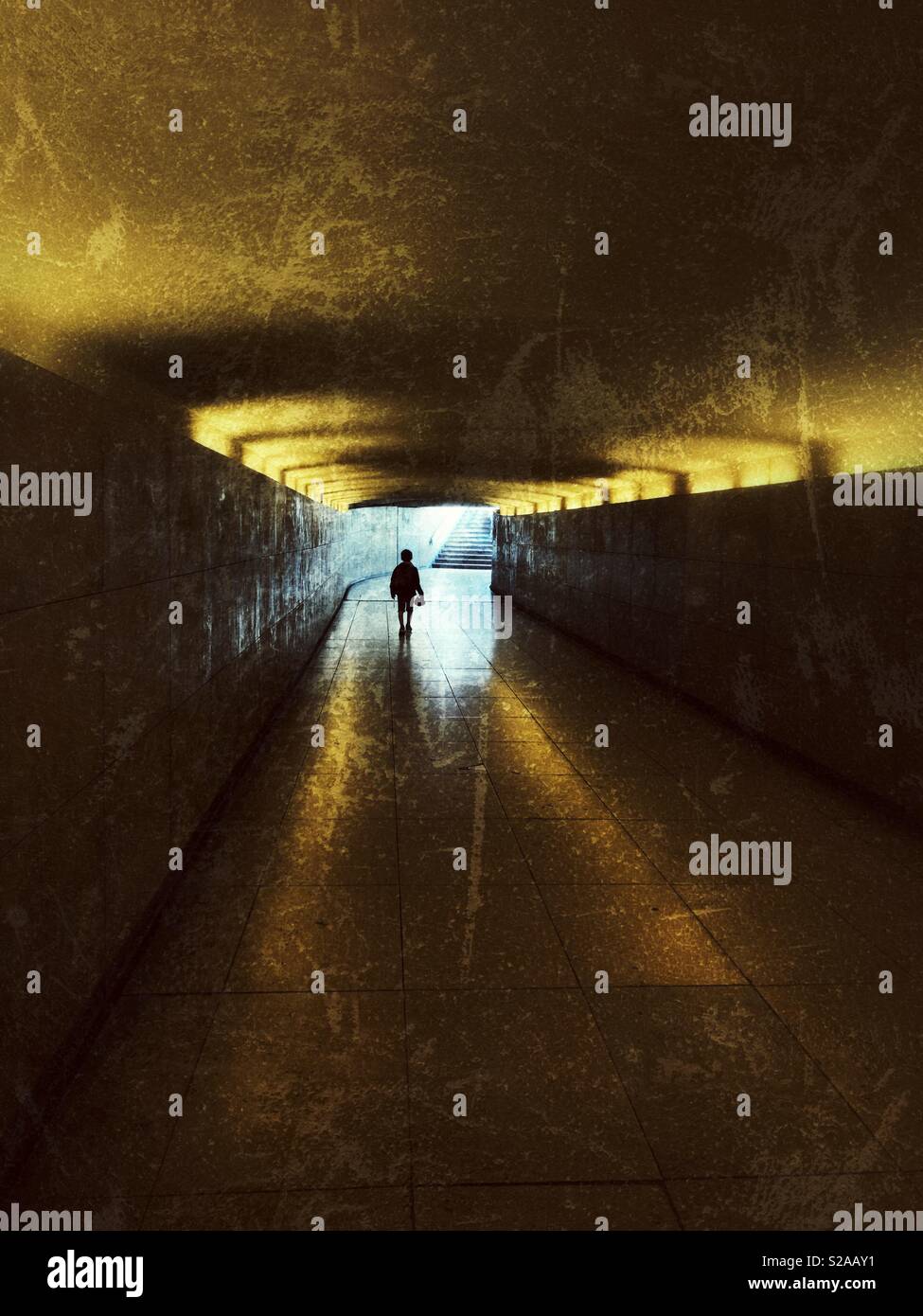 Boy walking a narrow tunnel with light at the end Stock Photo