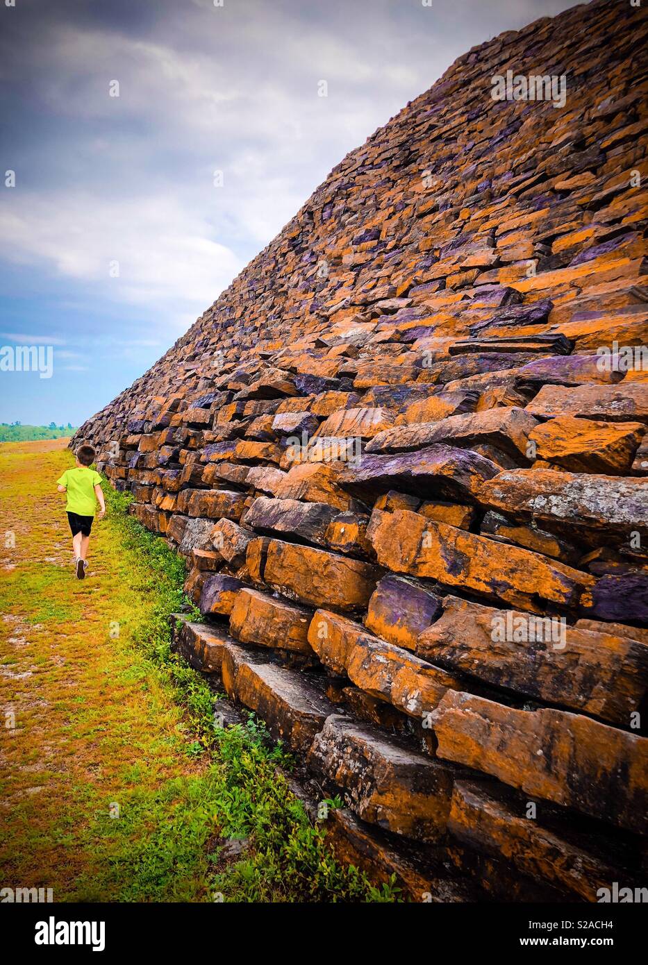 An eight year old walks along the bottom of a large rock structure away from the camera. - Smartphone Captured Stock Image