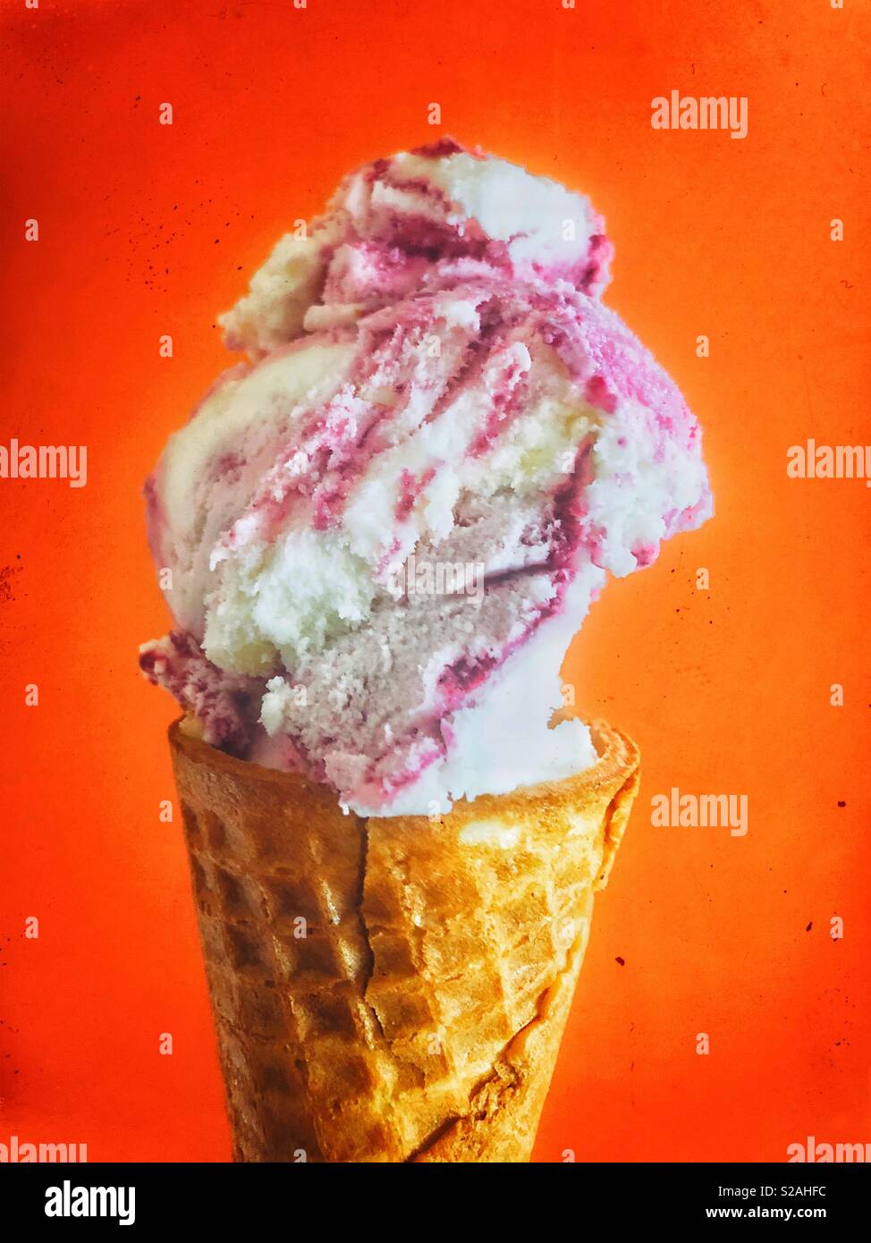 Closeup of raspberry ice cream in a waffle cone on bright orange red background - Smartphone Captured Stock Image