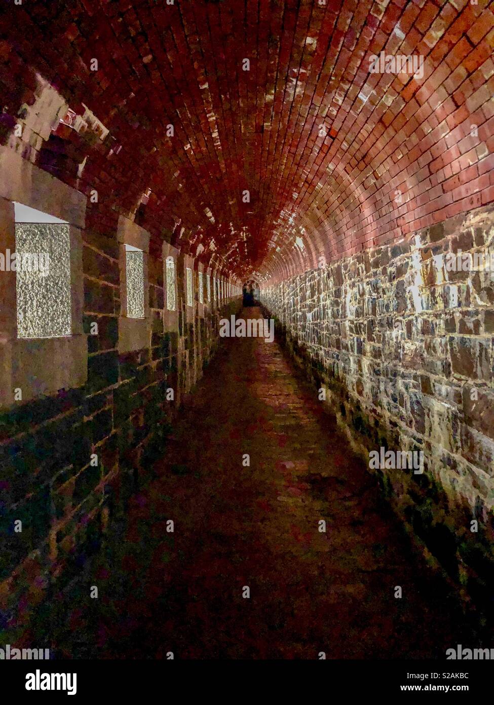 A brick tunnel leader off into the distance. Sunlight streams through a row of windows along one wall. - Smartphone Captured Stock Image