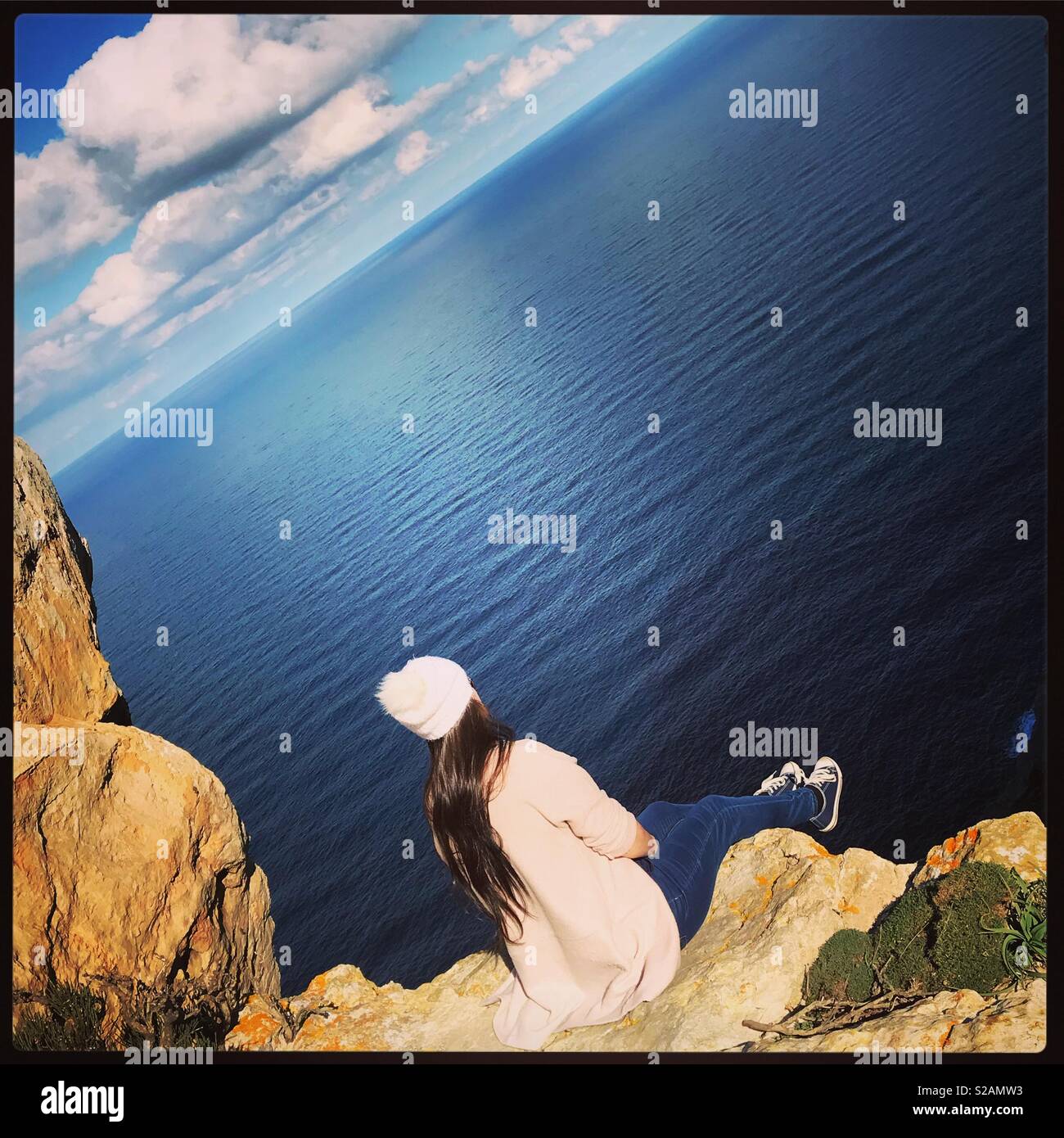 Woman sat on edge of cliff looking out to sea Stock Photo - Alamy