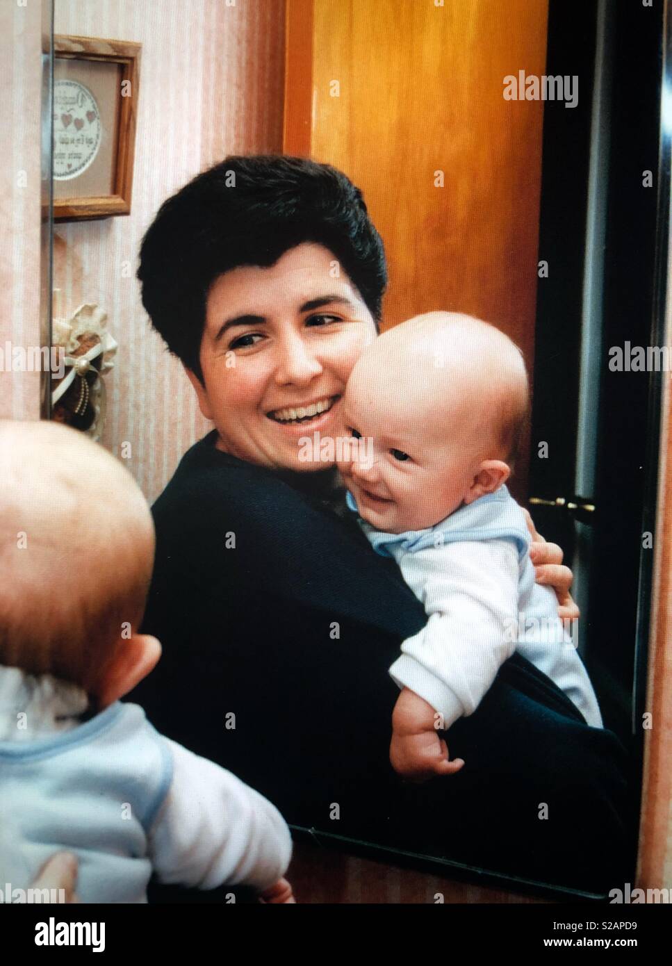 A mother holds her baby boy in front of a mirror to see how s reflection - Smartphone Captured Stock Image