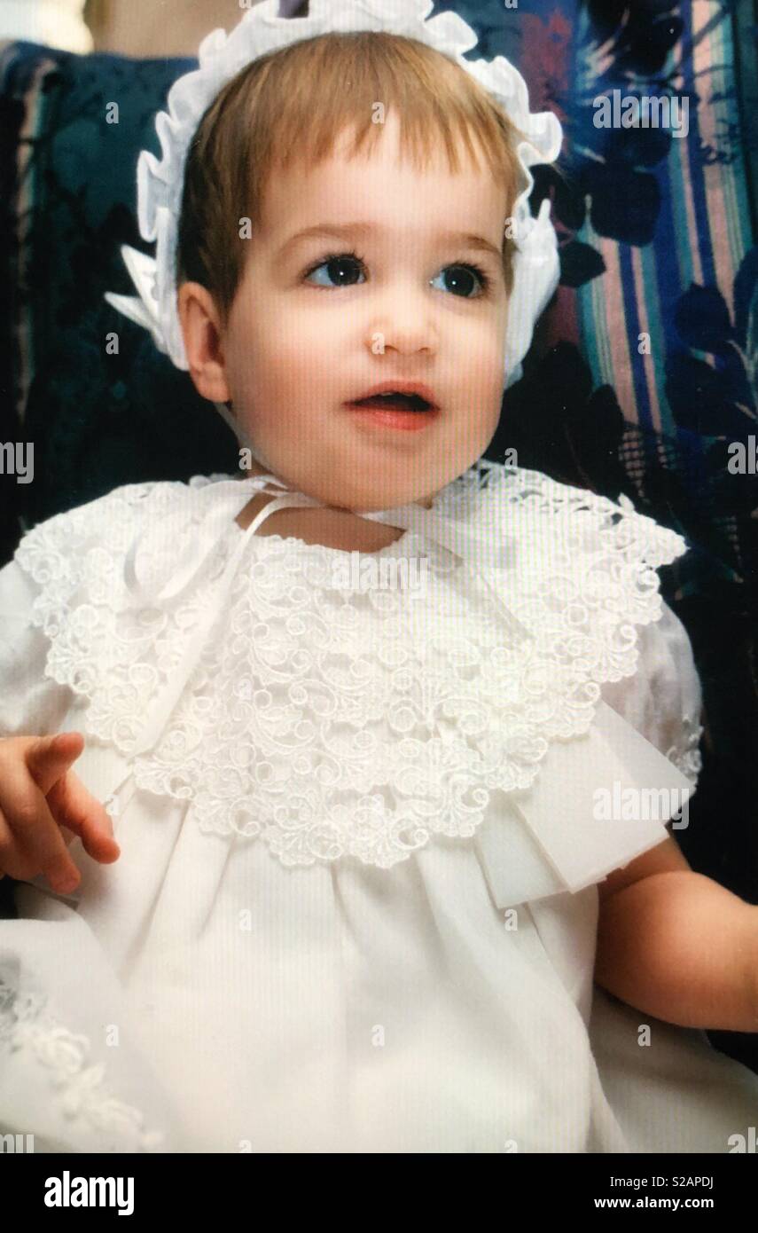 A closeup portrait of a baby girl dressed in a white dress and hat Stock Photo