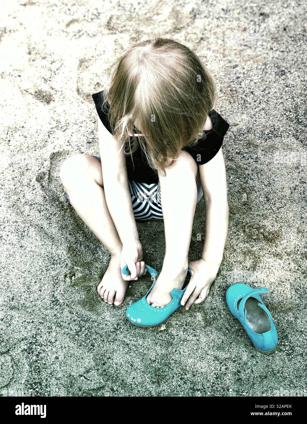 2 year old little girl sitting in sand putting her shoes on Stock Photo
