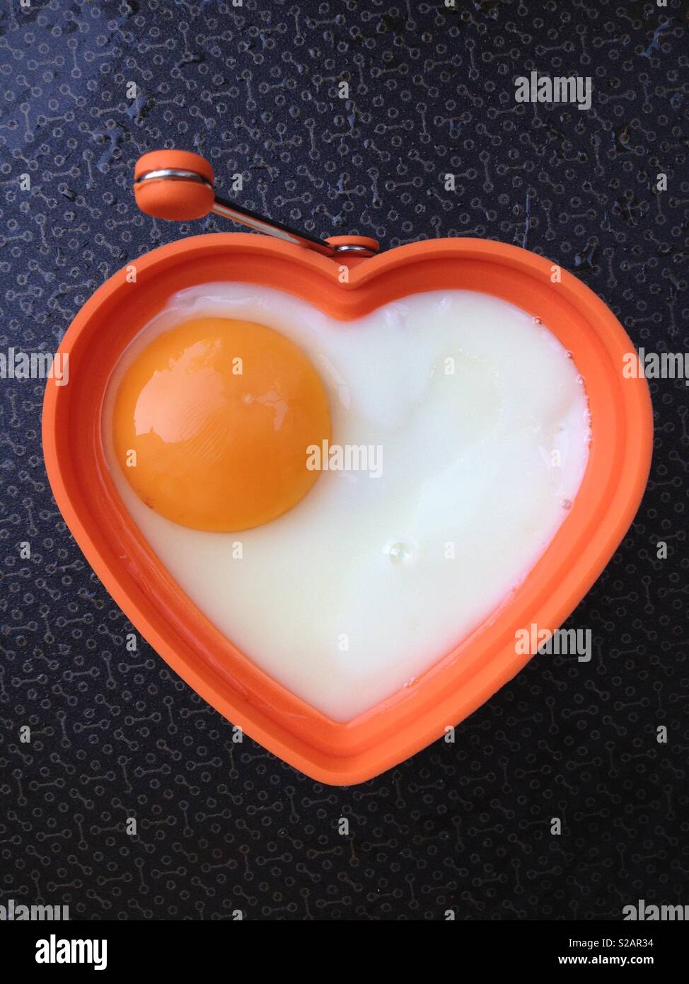 Fried egg being fried / frying in a frying pan. The eggs is in the shape of a healthy heart to imply a healthy diet and good well being. Stock Photo