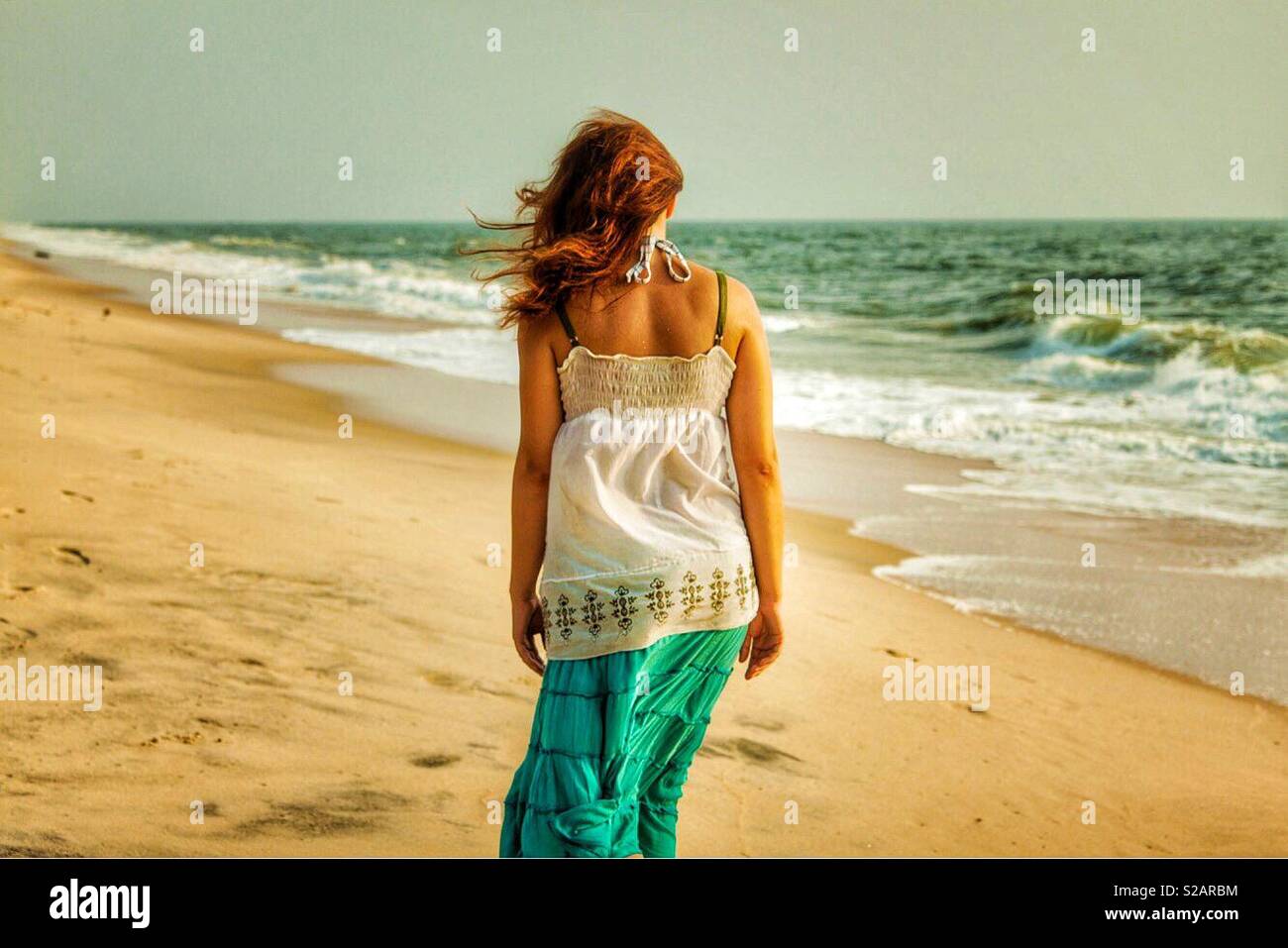 Young woman, back view, walking along the beach in India - Smartphone Captured Stock Image