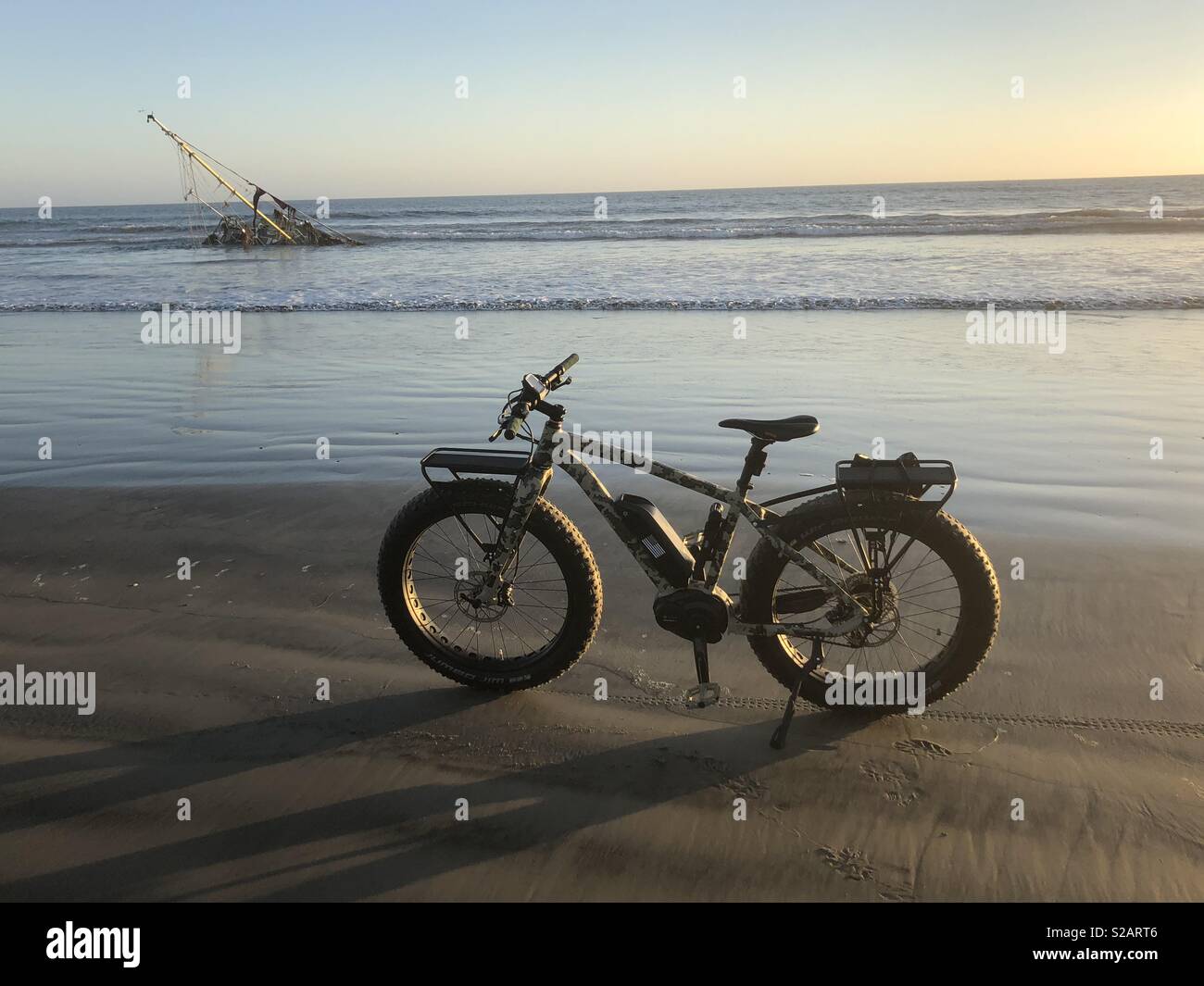 A fat tire bicycle on the beach with the ocean and a wrecked sailboat in the background near sunset. - Smartphone Captured Stock Image