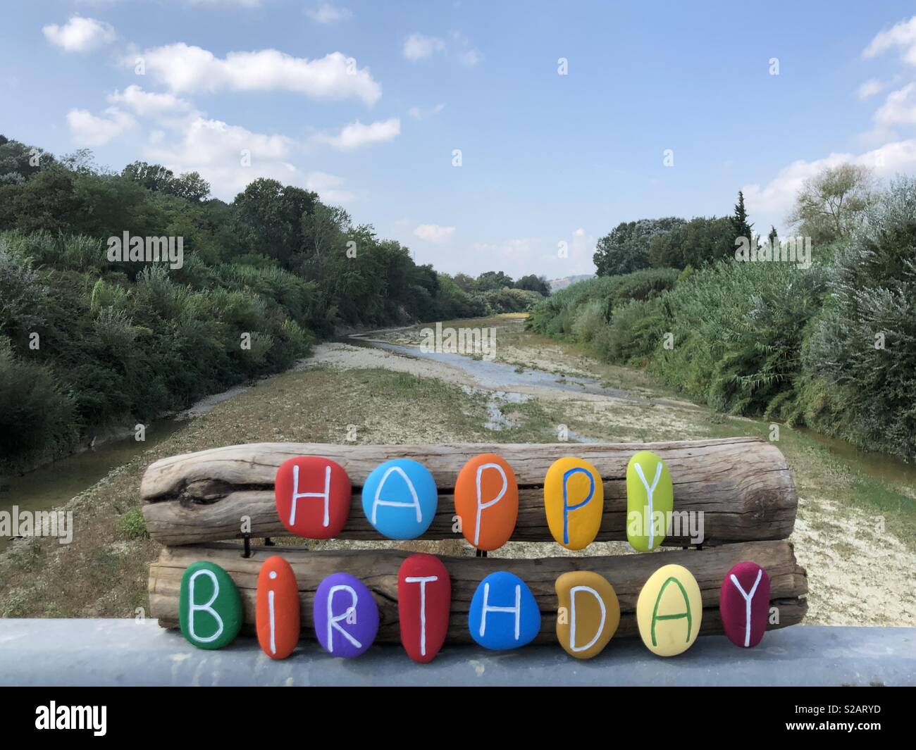 Happy Birthday message with colored stones over pieces of wood and dry river background - Smartphone Captured Stock Image
