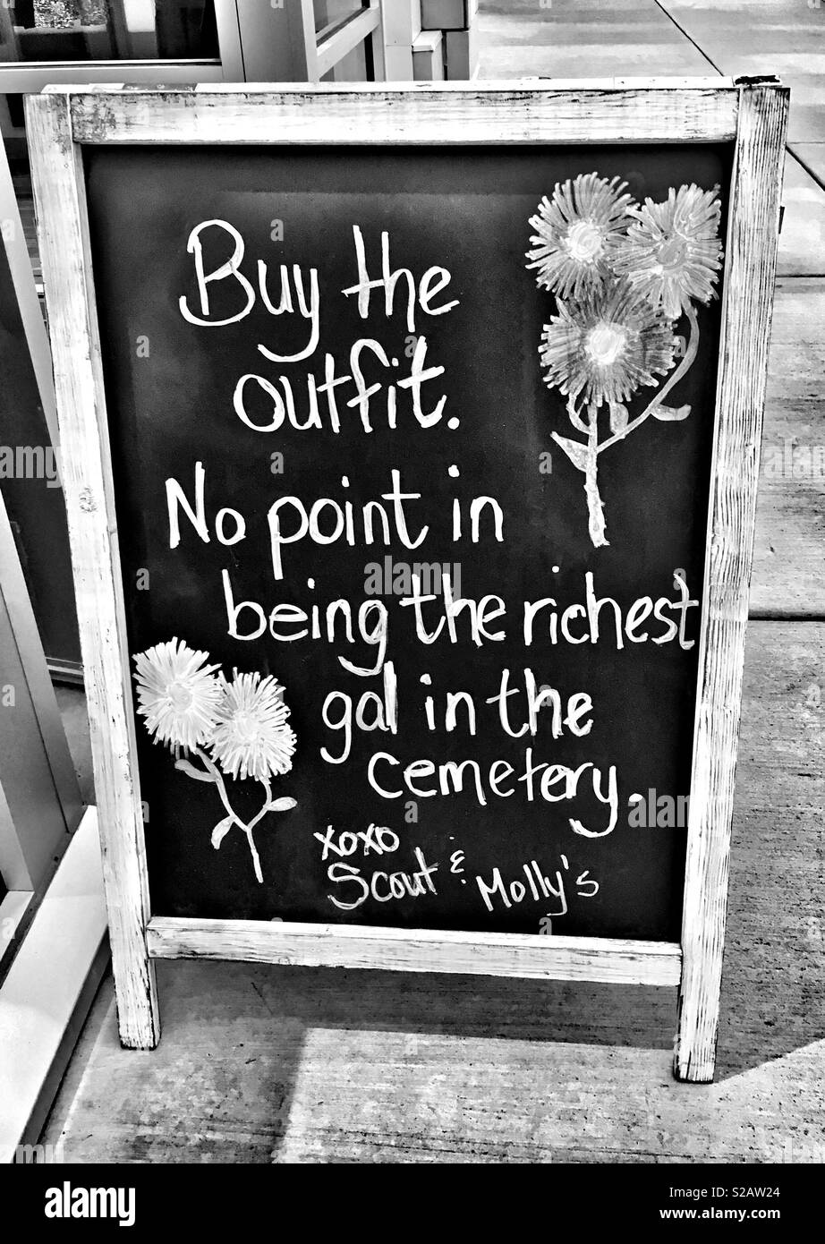 Chalkboard writing outside of store: Buy the outfit, no point in being the richest gal in the cemetery Stock Photo
