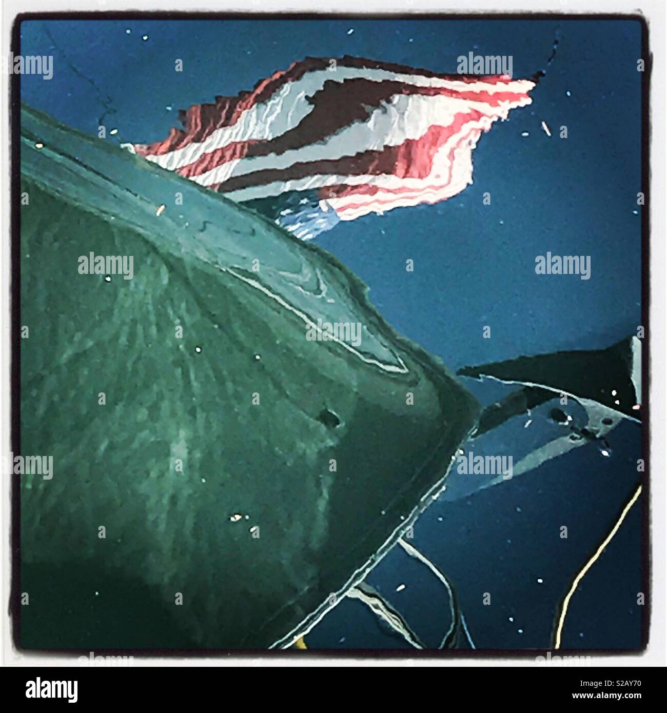 Reflections of an American flag and the bow of a boat on the surface of the water. Stock Photo
