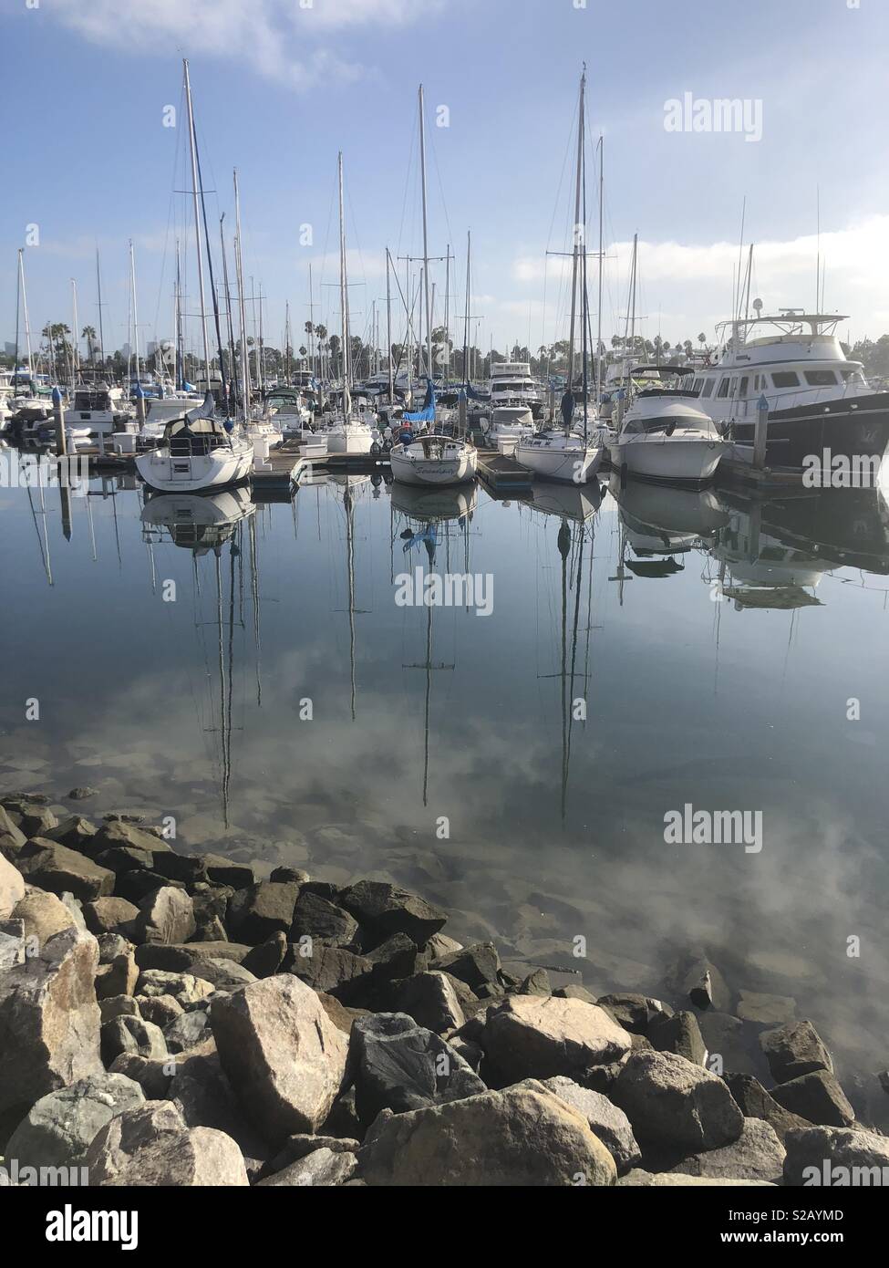 Sailboats sit in a placid bay with reflecting images on the water. - Smartphone Captured Stock Image