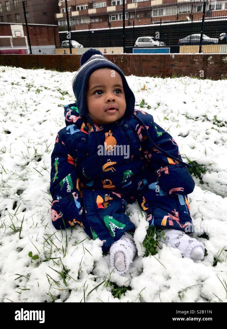 Black many boy wearing a snow suit sitting on grass covered by snow Stock Photo Alamy