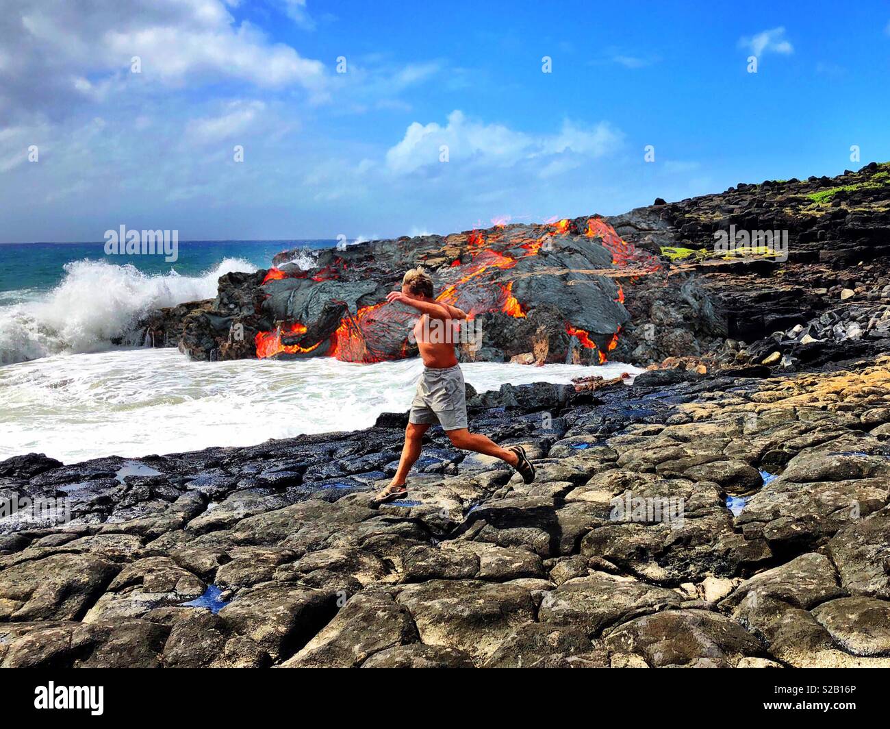 Man running towards shore amidst fiery lava flow in Hawaii - Smartphone Captured Stock Image