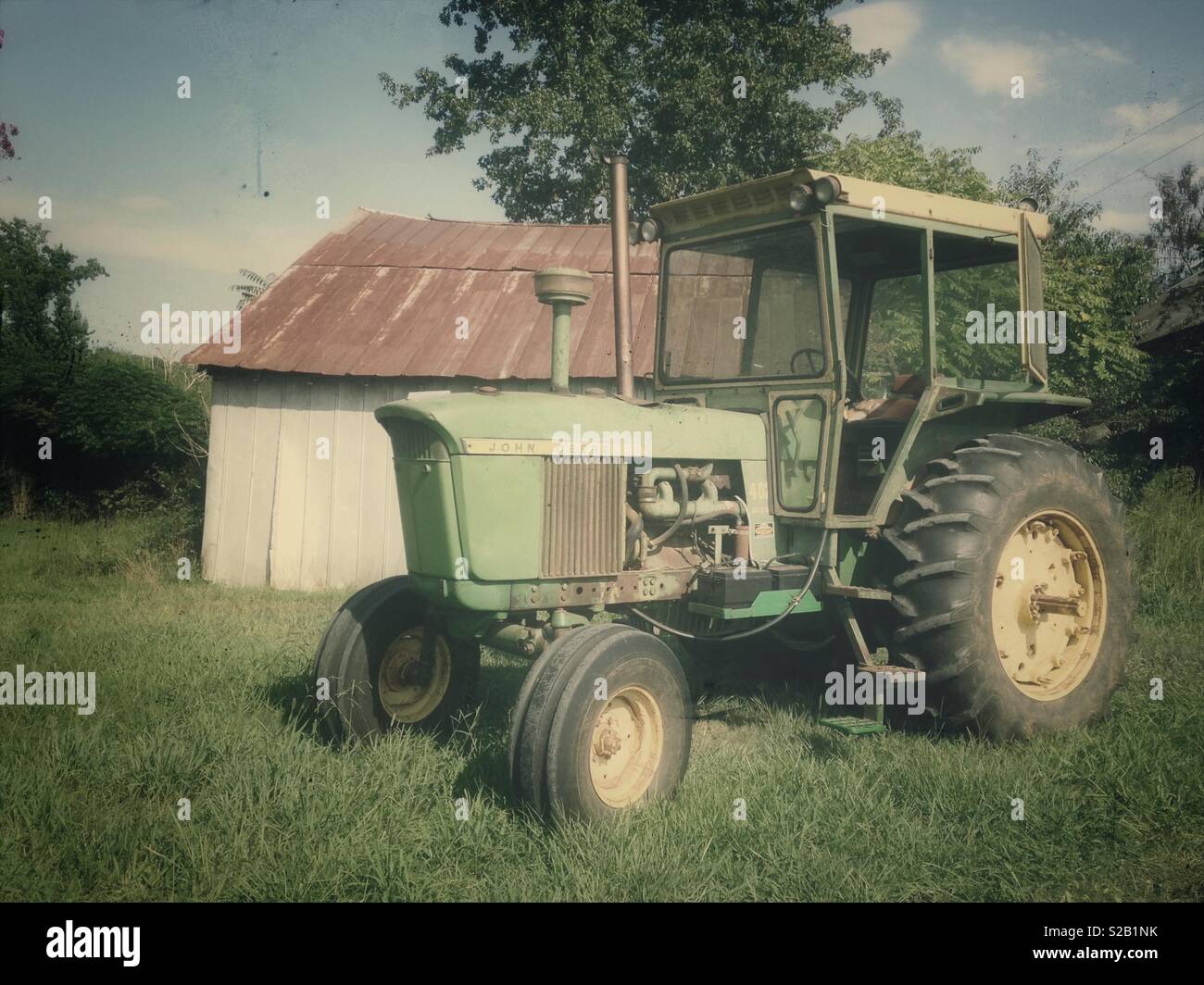Vintage photo of old John Deere 4020 tractor with cab parked by rusted tin shed Stock Photo