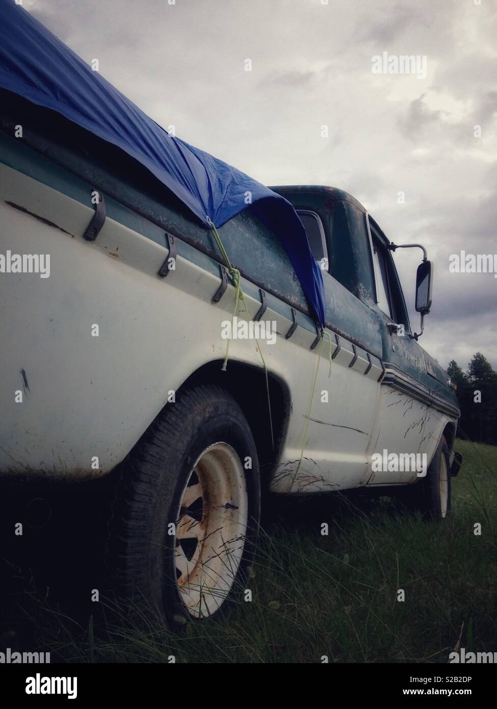 Low angle portrait photo of classic green and white pickup with overcast sky above Stock Photo