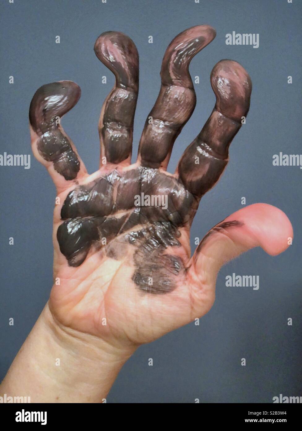 An abstract digital manipulation showing a hand covered in grey paint with distorted fingers Stock Photo