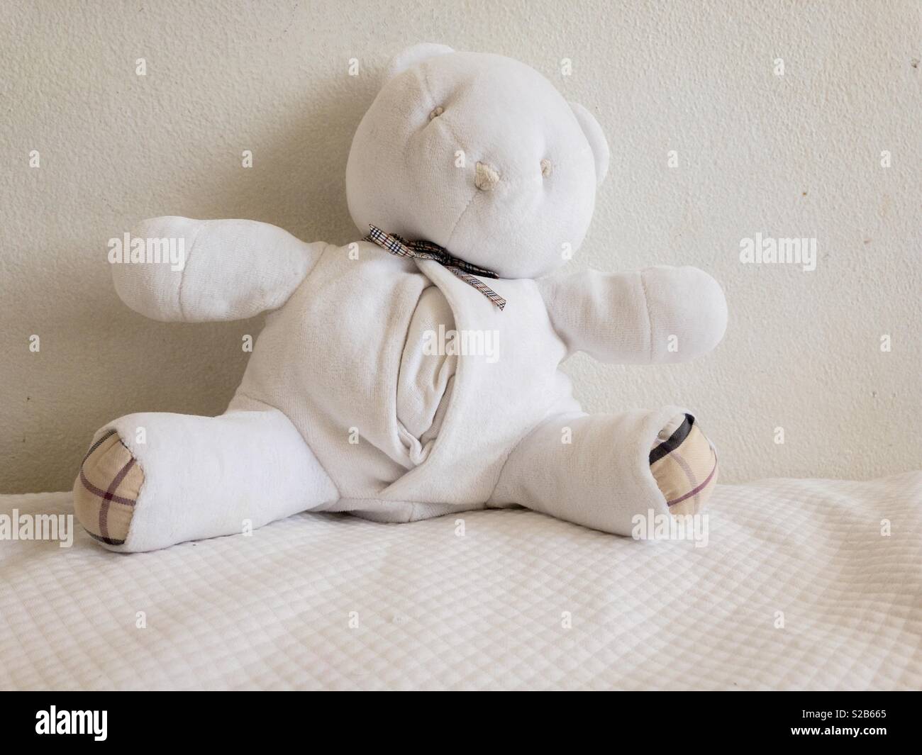 White teddy bear on a white bedcover against a white wall. - Smartphone Captured Stock Image