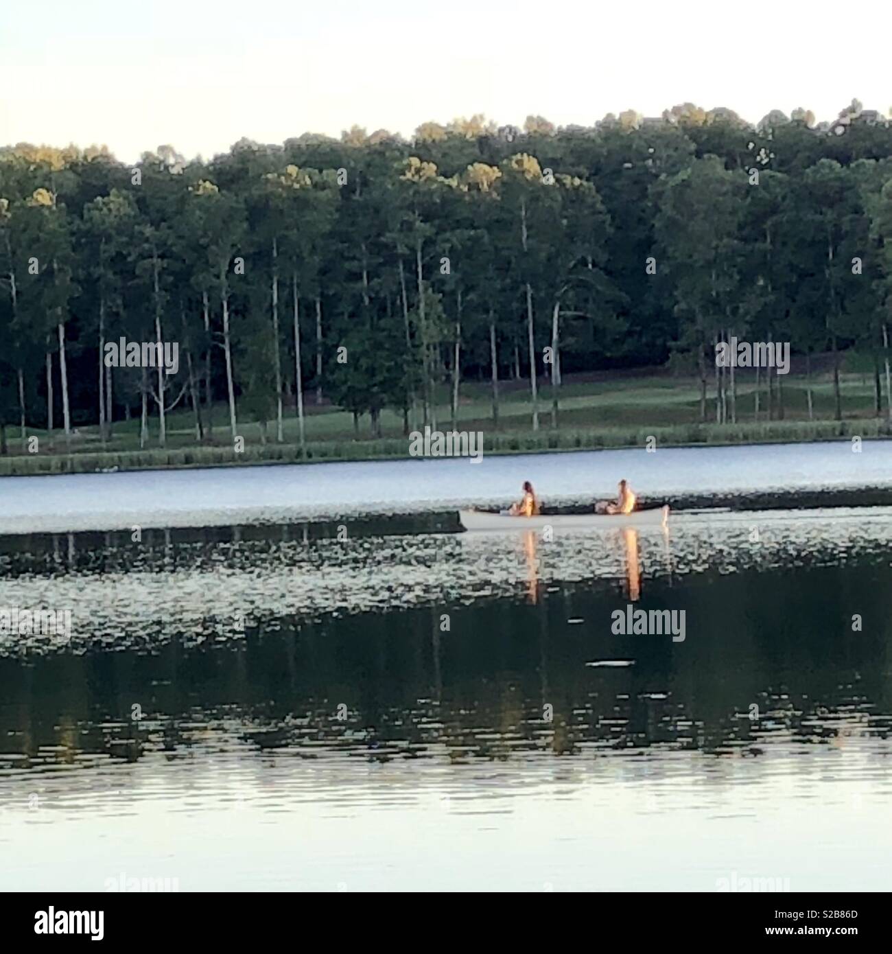 Canoe on lake at sunset with reflections of 2 people in the lake. Stock Photo