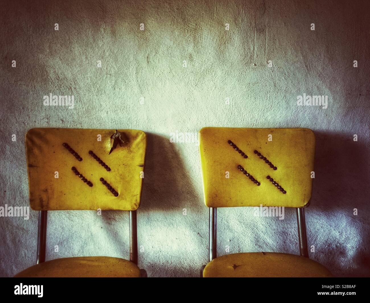 Tattered yellow vintage kitchen chairs against a blank wall - Smartphone Captured Stock Image